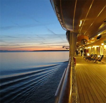 A cruise ship deck with chairs and tables on the side.