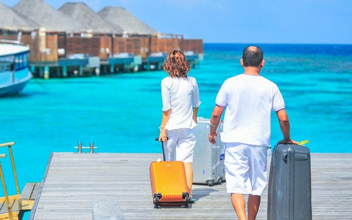 A man and woman walking on the pier with luggage.